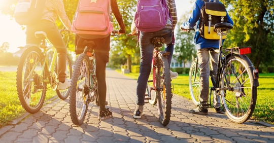 four kids wearing backpacks sitting on bicycles on a sidewalk