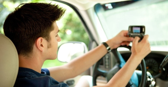 teenage boy sitting in the driver's seat with both hands typing on a phone