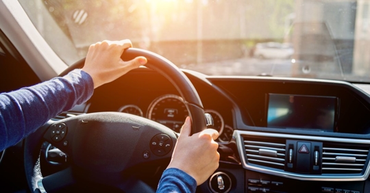person wearing long sleeves sitting in the driver's seat of a car with their hands on the steering wheel in a turning motion