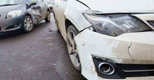 a white car with a damaged front bumper in front of a small blue car with a dented side