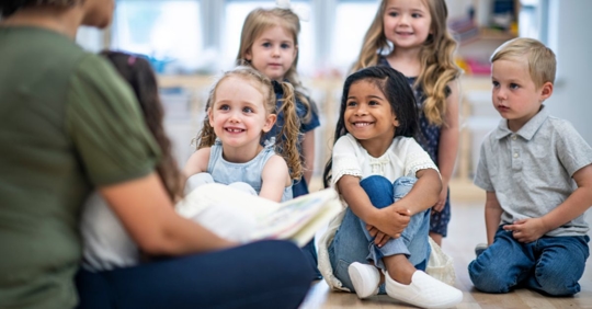 group of young children sitting on the floor across from an adult woman in a daycare center